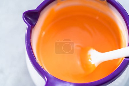 Photo for Melting color chocolate chips in a candy melting pot to make carrot chocolate-covered pretzels. - Royalty Free Image