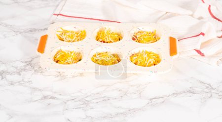 Téléchargez les photos : Remplir le moule à muffins en silicone avec des ingrédients pour cuire le bacon et le muffin aux œufs au fromage. - en image libre de droit