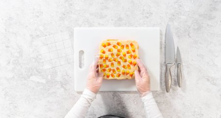 Photo for Flat lay. Scoring candy corn fudge using a parchment paper template for cutting into small pieces. - Royalty Free Image