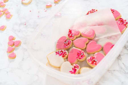 Téléchargez les photos : Stockage de biscuits au sucre en forme de cœur avec glaçage royal rose et blanc dans un grand récipient en plastique. - en image libre de droit