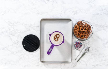 Téléchargez les photos : Flat lay. Dipping pretzels twists into melted chocolate to make red, white, and blue chocolate-covered pretzel twists. - en image libre de droit