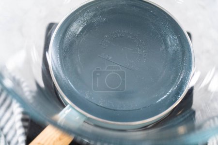Téléchargez les photos : Faire fondre les pépites de chocolat blanc et d'autres ingrédients dans un bol de mélange en verre sur de l'eau bouillante pour préparer le caramel à la pistache aux canneberges. - en image libre de droit