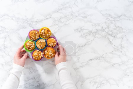 Foto de Acostado. Magdalenas de semilla de amapola de limón recién horneadas adornadas con astillas de almendras en el mostrador de la cocina. - Imagen libre de derechos