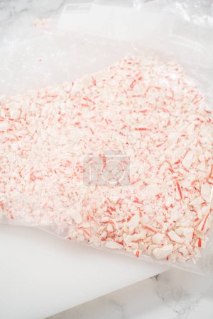 Foto de Triturar caramelos de menta en una bolsa de plástico con un rodillo de mármol en una tabla de cortar blanca. - Imagen libre de derechos