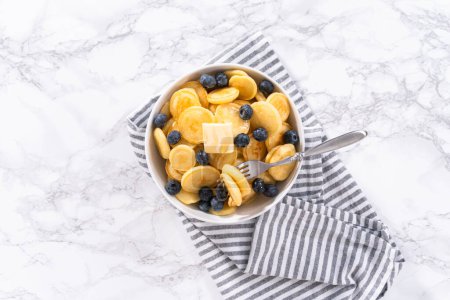 Téléchargez les photos : Pose plate. Mini céréales crêpes fraîchement préparées avec des bleuets frais dans un bol blanc. - en image libre de droit