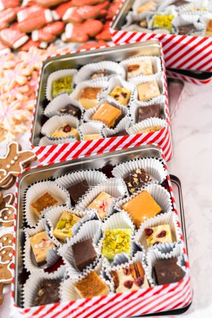 Photo for Packaging a homemade variety of fudge and gingerbread cookies for Christmas food gifts into tin boxes. - Royalty Free Image