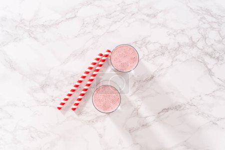 Photo for Flat lay. Freshly made healthy breakfast strawberry banana smoothie garnished with fresh strawberry and paper straw. - Royalty Free Image
