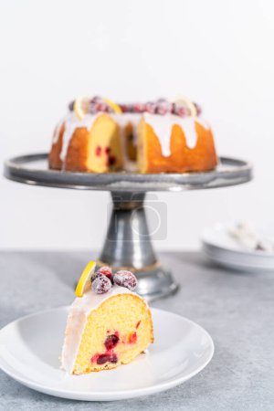 Téléchargez les photos : Gâteau de lapin de canneberge au citron tranché décoré de canneberges à sucre et de quartiers de citron sur un stand de gâteau. - en image libre de droit