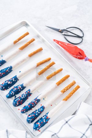 Photo for Dipping pretzel rods into the melted chocolate to prepare chocolate dipped pretzel rods for the July 4th celebration. - Royalty Free Image
