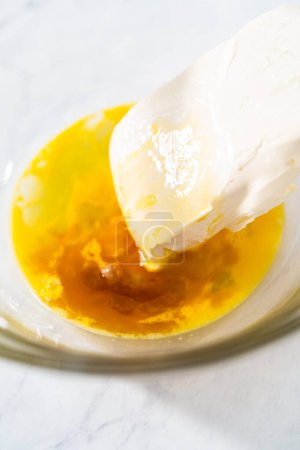 Téléchargez les photos : Mélanger les ingrédients dans un grand bol de mélange en verre pour faire la garniture de fromage à la crème pour gâteau bundt. - en image libre de droit