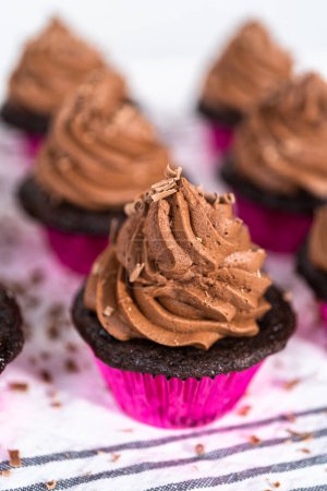 Téléchargez les photos : Piping chocolat ganache glaçage sur le dessus de cupcakes au chocolat. - en image libre de droit