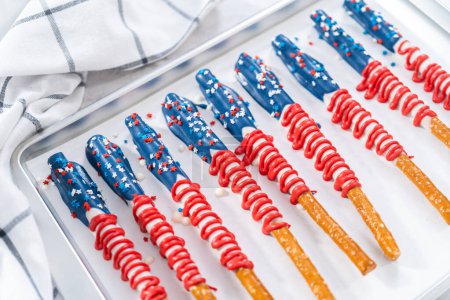 Téléchargez les photos : Bâtonnets de bretzels faits maison recouverts de chocolat décorés comme le drapeau américain séchant sur une plaque à pâtisserie tapissée de papier parchemin. - en image libre de droit