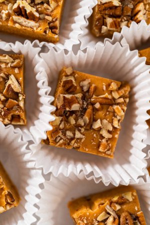 Photo for Homemade pumpkin spice fudge square pieces in white paper cupcake liners on a kitchen counter. - Royalty Free Image