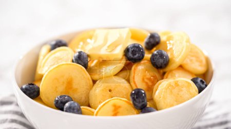 Photo for Step by step. Freshly made mini pancake cereal with fresh blueberries in a white bowl. - Royalty Free Image