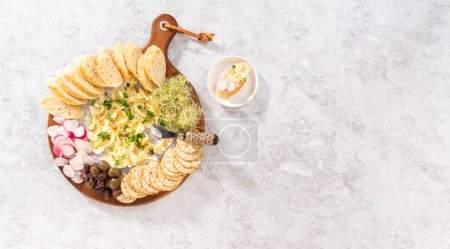 Foto de Acostado. Tabla de mantequilla con verduras y pan en una tabla de cortar de madera redonda. - Imagen libre de derechos