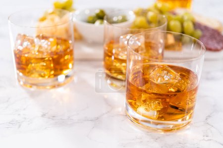 Photo for Scotch on the rocks in whiskey glass on a white marble surface. - Royalty Free Image