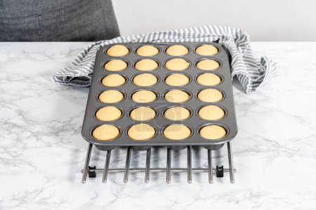 Foto de Enfriamiento recién horneado mini cupcakes de vainilla en un mostrador de cocina. - Imagen libre de derechos