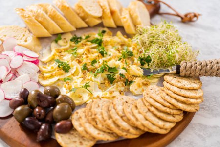 Foto de Tabla de mantequilla con verduras y pan en una tabla de cortar de madera redonda. - Imagen libre de derechos