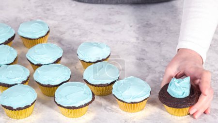 Foto de Paso a paso. Recoger glaseado de crema de mantequilla azul en la parte superior de los cupcakes de chocolate. - Imagen libre de derechos