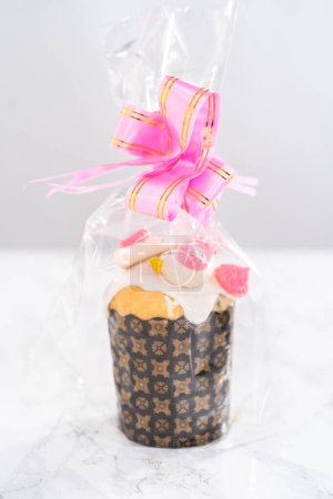 Téléchargez les photos : Mini koulich de pain de Pâques enveloppé avec glaçure au citron, décoré avec des saupoudres et des biscuits meringue en forme d'oiseau comme un bon cadeau. - en image libre de droit