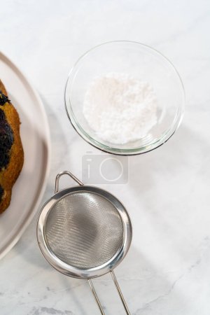 Téléchargez les photos : Saupoudrer le gâteau de lapin de myrtille au citron fraîchement cuit avec du sucre en poudre. - en image libre de droit