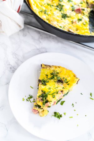 Photo for Slice of spinach and ham frittata on a white dinner plate. - Royalty Free Image