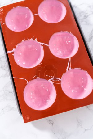 Foto de Rellenar moldes de chocolate de silicona con chocolate rosa derretido para preparar bombas de chocolate caliente. - Imagen libre de derechos