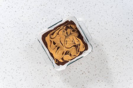 Téléchargez les photos : Pose plate. Verser le mélange de caramel dans le moule tapissé de papier sulfurisé pour préparer le caramel au chocolat avec tourbillon de beurre d'arachide. - en image libre de droit
