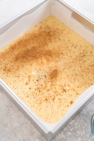 Photo for Pouring fudge mixture into the square cheesecake pan lined with parchment paper to prepare eggnog fudge. - Royalty Free Image