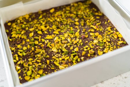 Photo for Removing chocolate pistachio fudge from a square cheesecake pan lined with parchment. - Royalty Free Image