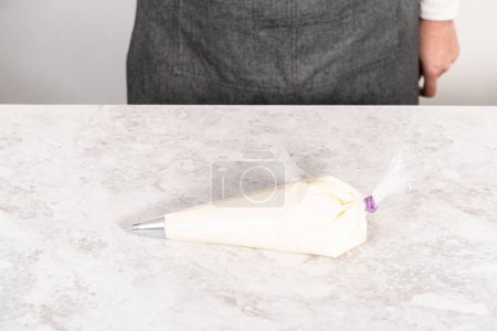 Téléchargez les photos : Glaçage blanc crème au beurre dans un sac de tuyauterie avec une pointe en métal. - en image libre de droit