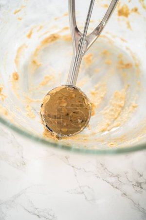 Photo for Scooping dough with dough scoop into cupcake pan lined with tulip paper muffin liners to bake banana oatmeal muffins. - Royalty Free Image