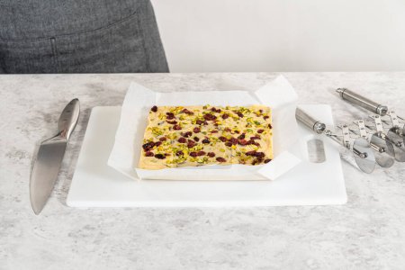 Téléchargez les photos : Enlever le caramel à la pistache aux canneberges d'une poêle à gâteau au fromage carrée doublée de parchemin. - en image libre de droit