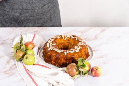 Photo for Slicing homemade apple bundt cake and garnishing with sliced almonds. - Royalty Free Image