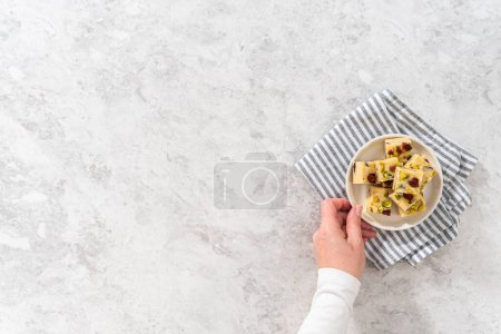 Photo for Flat lay. Homemade cranberry pistachio fudge square pieces on a white plate. - Royalty Free Image