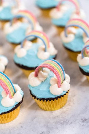 Téléchargez les photos : Cupcakes au chocolat décorés avec glaçage bleu crème au beurre et arc-en-ciel pour fête d'anniversaire thème licorne. - en image libre de droit