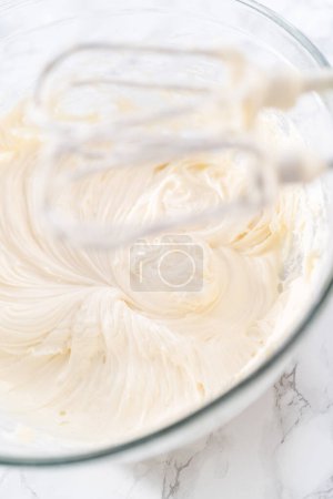 Photo for Mixing ingredients in a large glass mixing bowl to prepare cream cheese frosting. - Royalty Free Image