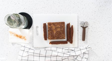 Foto de Acostado. Cortar la mantequilla de cacahuete de chocolate en trozos pequeños en una tabla de cortar blanca. - Imagen libre de derechos