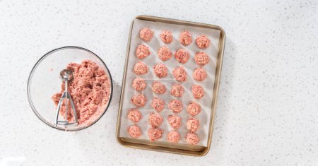 Photo for Flat lay. Scooping ground meat with dough scoop into a baking sheet lined with parchment paper to prepare oven-baked meatballs. - Royalty Free Image