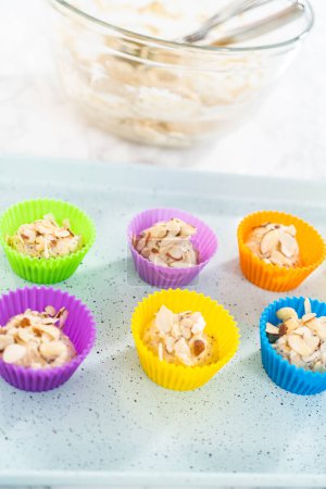 Téléchargez les photos : Cueillette de pâte à cupcake avec cuillère à pâte dans des doublures de muffins de silicium aux muffins de graines de pavot citron. - en image libre de droit