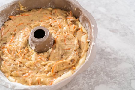 Téléchargez les photos : Remplissage casserole de gâteau bundt en métal avec du beurre de gâteau pour cuire le gâteau bundt carotte avec glaçage au fromage à la crème. - en image libre de droit