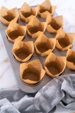 Téléchargez les photos : Ramasser la pâte dans la casserole à cupcake doublée de doublures de muffins en parchemin pour cuire des muffins sharlotka. - en image libre de droit