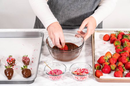 Photo for Dipping strawberries into the melted chocolate to prepare chocolate-covered strawberries. - Royalty Free Image