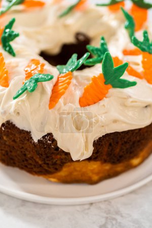 Téléchargez les photos : Décorer gâteau bundt aux carottes fraîchement cuit avec glaçage au fromage à la crème avec garnitures gâteau aux carottes au chocolat. - en image libre de droit