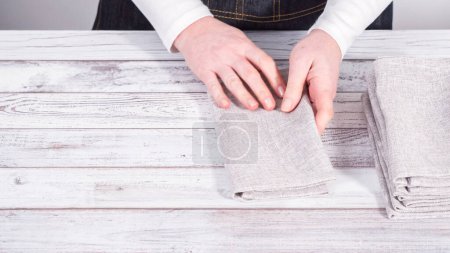 Photo for Step by step. Folding natural color linen dinner napkin on a wooden white table. - Royalty Free Image