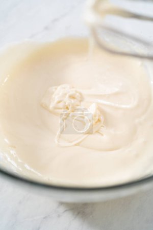 Photo for Mixing ingredients in a large glass mixing bowl to make the cream cheese glaze. - Royalty Free Image