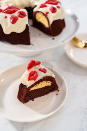 Foto de Slicing freshly baked red velvet bundt cake with chocolate lips and hearts over cream cheese glaze for Valentines Day. - Imagen libre de derechos