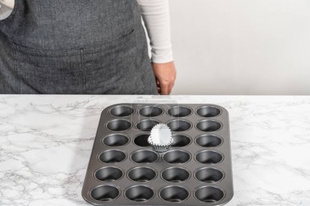 Téléchargez les photos : Scooping cupcake batter with dough scoop into a baking pan with liners to bake American flag mini cupcakes. - en image libre de droit