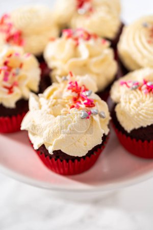Téléchargez les photos : Cupcakes de velours fraîchement cuits au four avec glaçage ganache au chocolat blanc décoré de saupoudres. - en image libre de droit