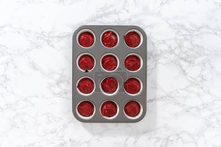 Photo for Flat lay. Scooping cupcake dough with dough scoop into cupcake pan lined with foil liners to bake red velvet cupcakes with white chocolate ganache frosting. - Royalty Free Image